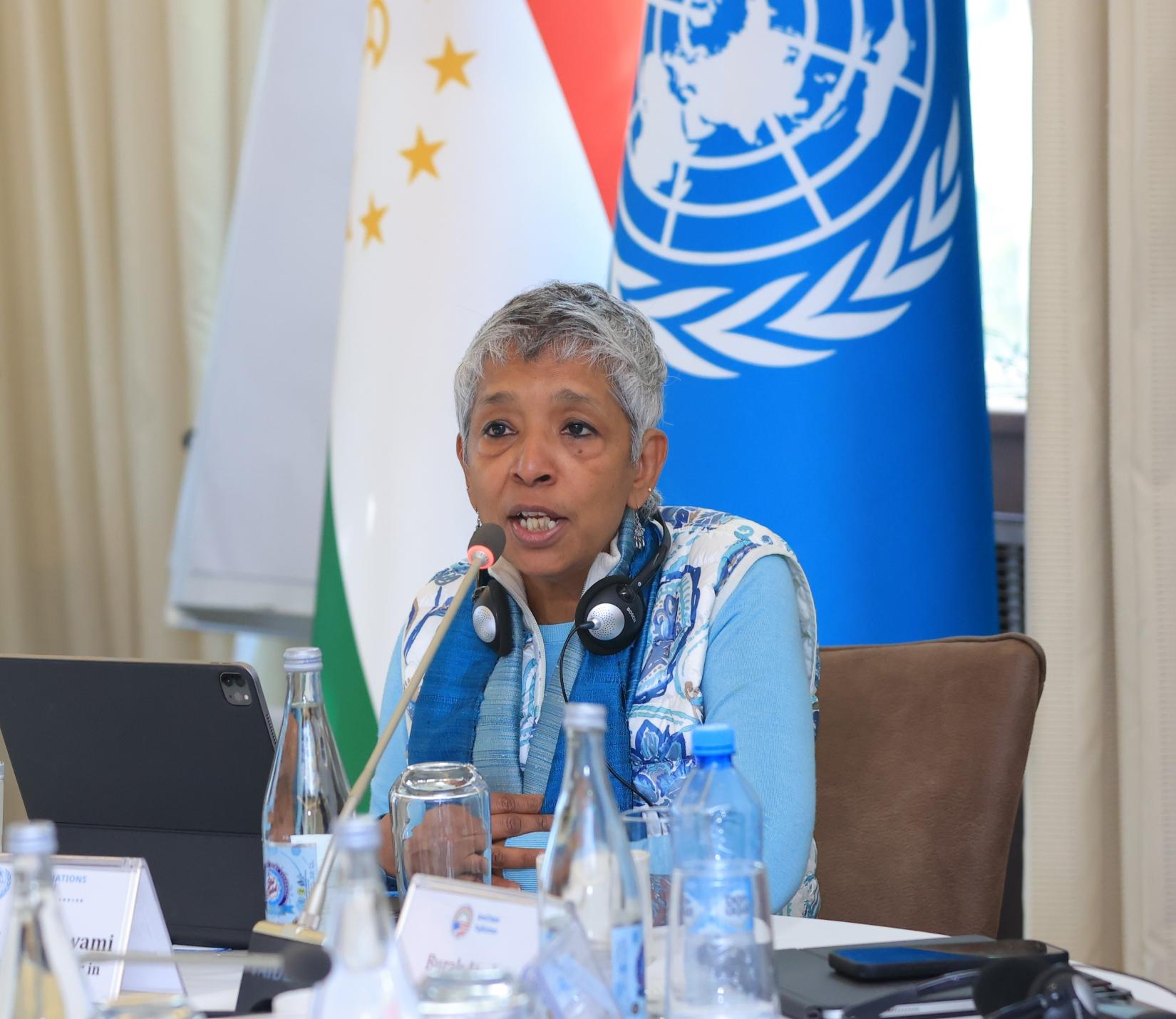 A woman sitting at the table speaks. Behind her Tajik and UN flags are visible